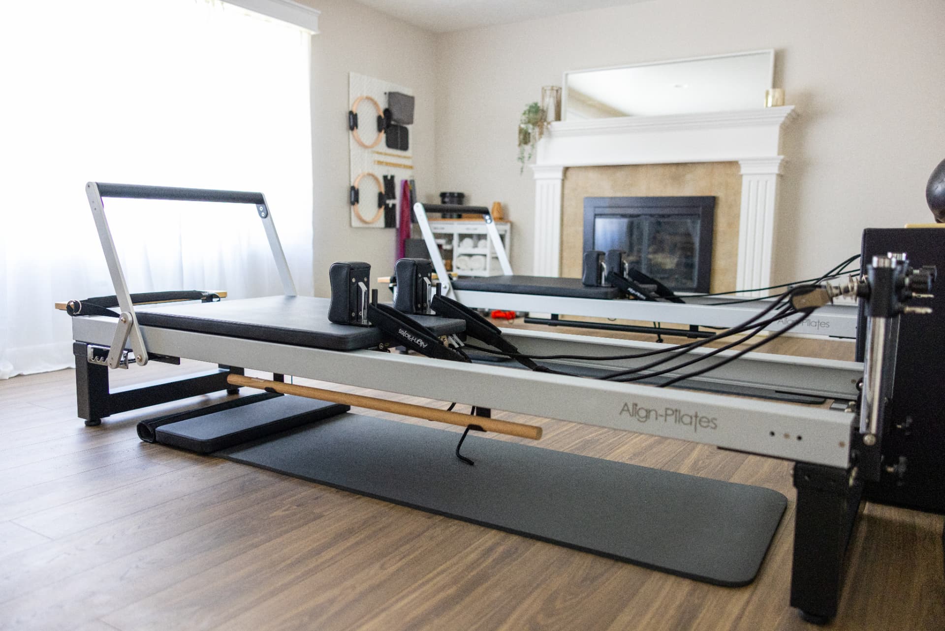 Two Align-Pilates reformers set up side by side in a bright studio room with a fireplace and window light